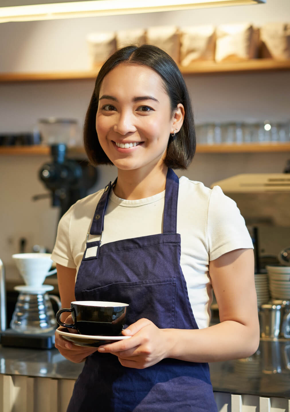 Young woman holding a coffee cup in a cafe wearing a white tshirt and an apron